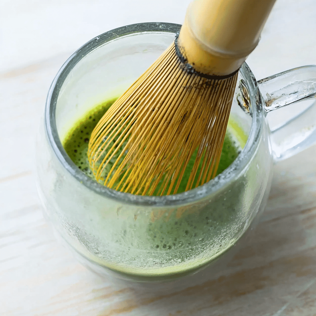 How to Make a Creamy Matcha Latte with Almond Milk 6 Bamboo matcha whisk mixing tea in a glass cup
