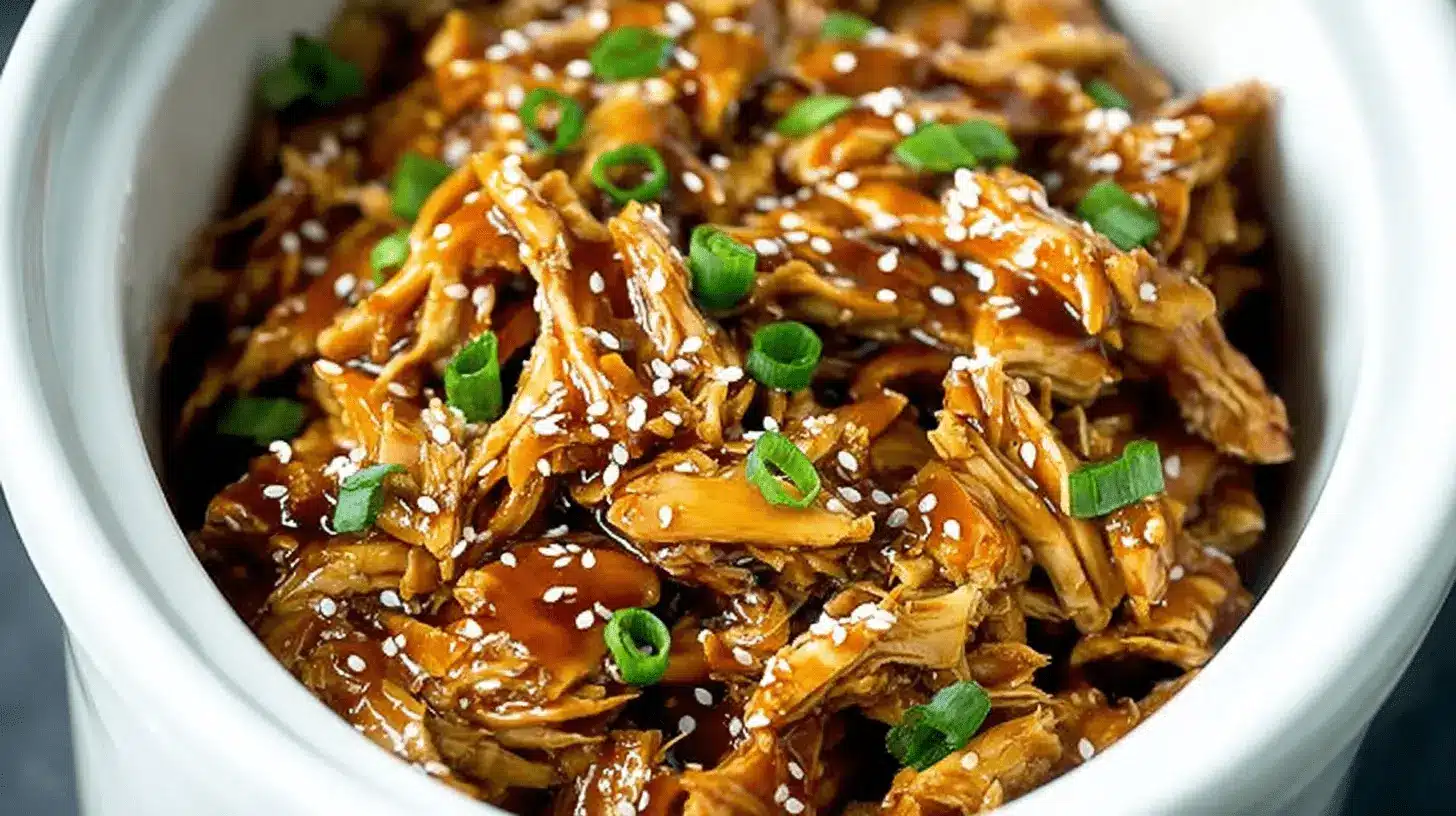 Close-up of glossy Slow Cooker teriyaki chicken garnished with sesame seeds and green onions.