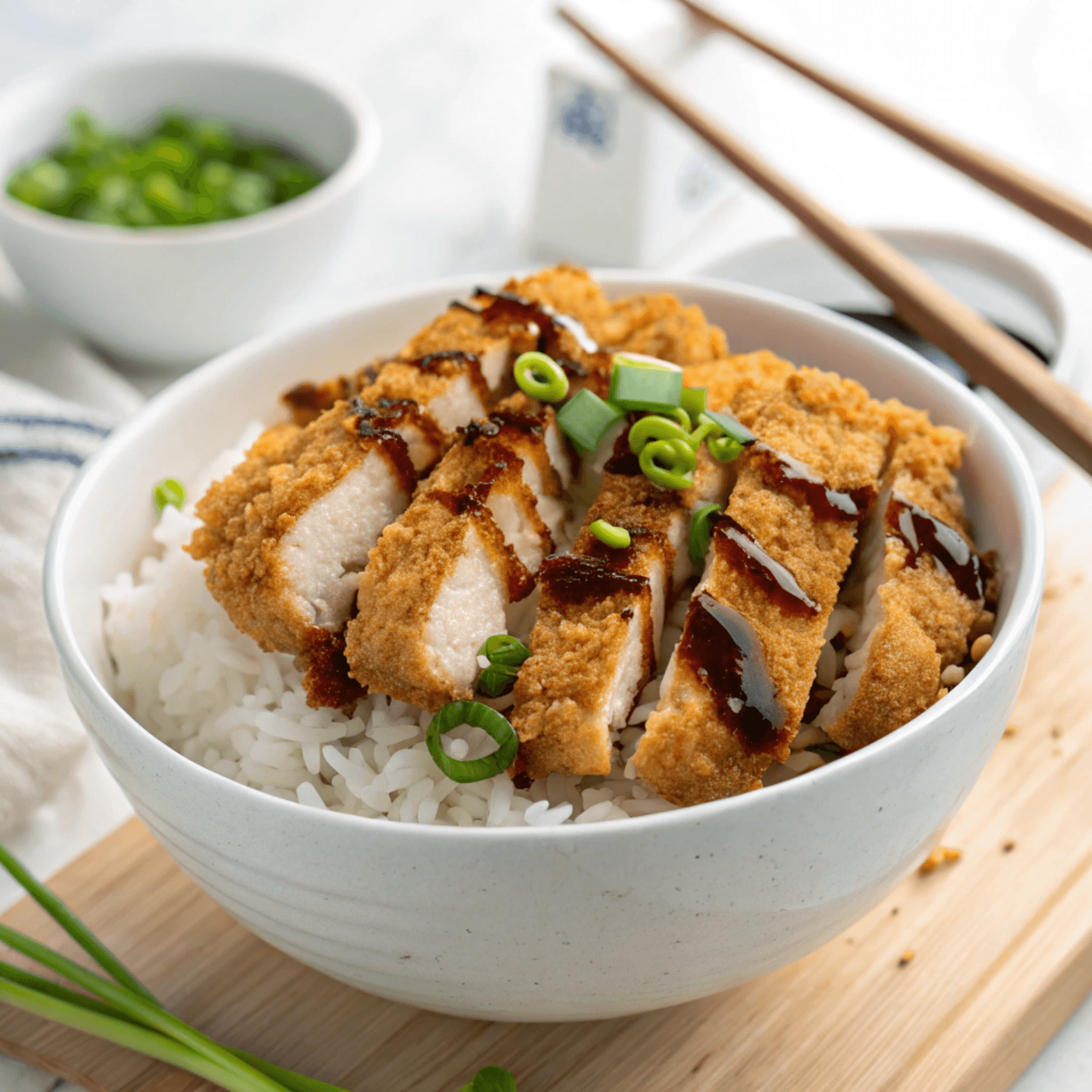 Japanese chicken katsu slices over rice with katsu sauce and green onions.