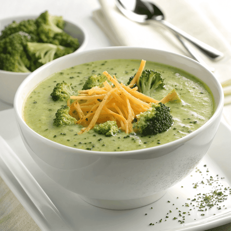 Broccoli cheddar soup served in a white bowl with melted cheese and broccoli florets