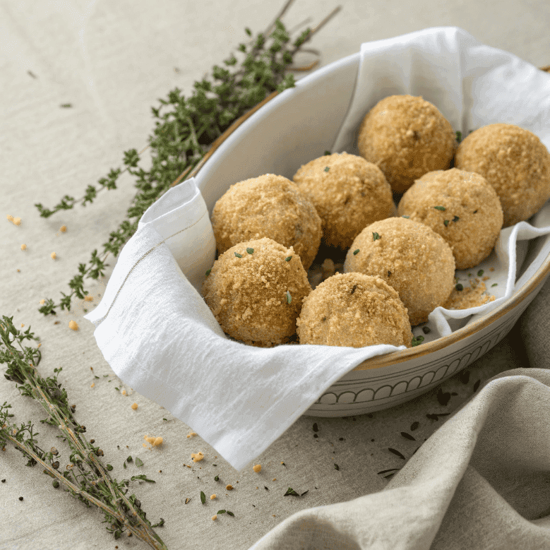 Full bowl of baked arancini rice balls with golden crust and thyme garnish